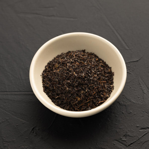 White bowl filled with dark brown Daintree tea leaves on a black textured background