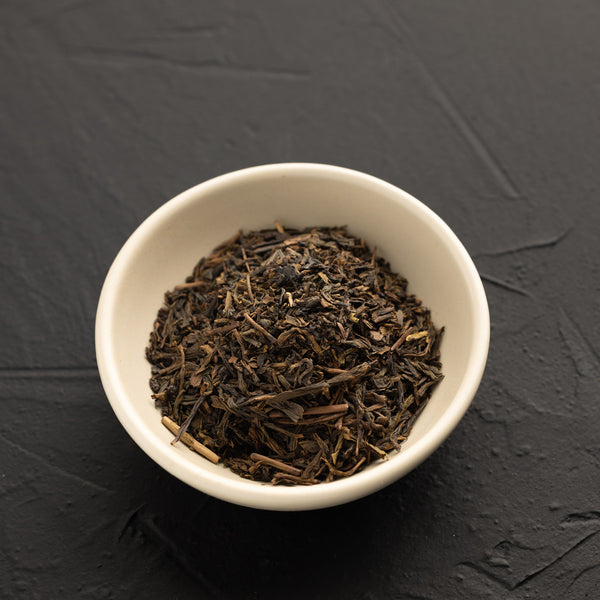 White bowl filled with dark brown Hojicha tea leaves on a black textured background