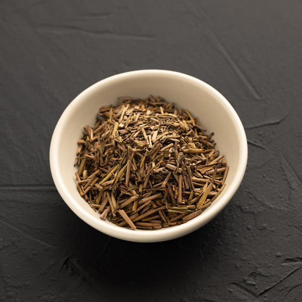 White bowl filled with dried Kuki Hojicha tea on a dark gray background