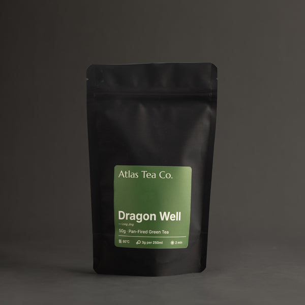 Black tea package with green label featuring 'Atlas Tea Co. Dragon Well' on a dark background