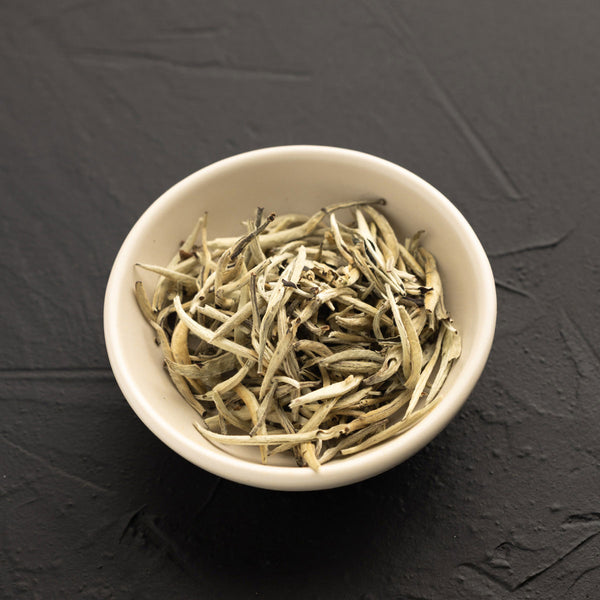 White bowl filled with dried tea leaves on a dark gray background