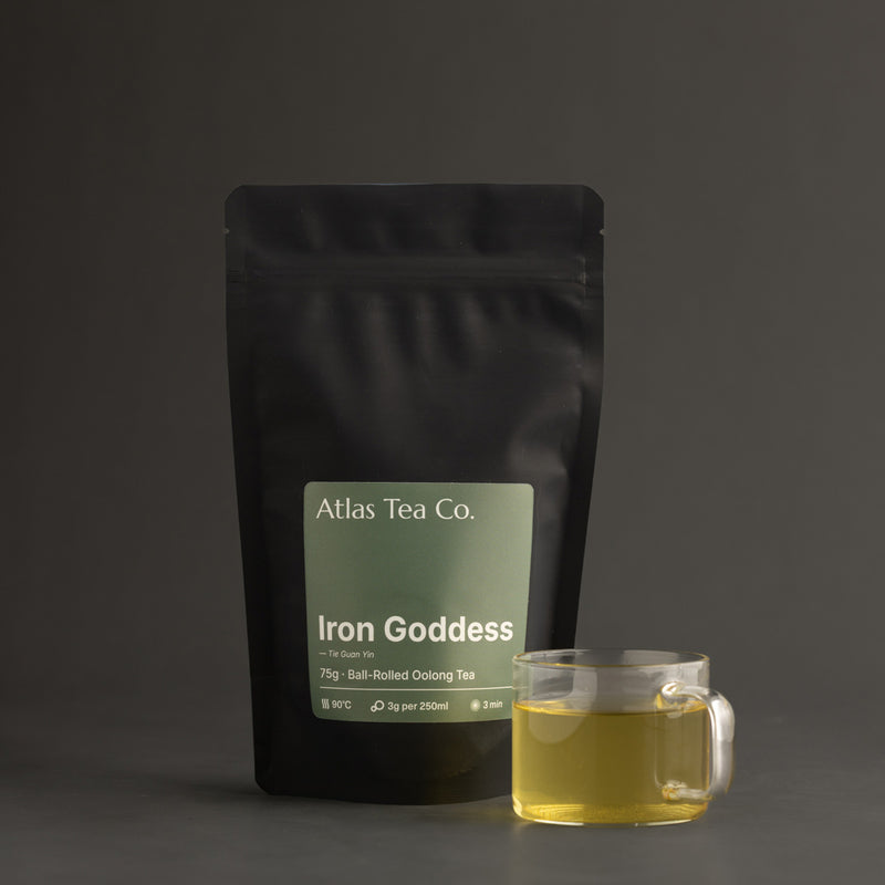 Tea package 'Iron Goddess' from Atlas Tea Co. with a glass mug of tea on a dark background.
